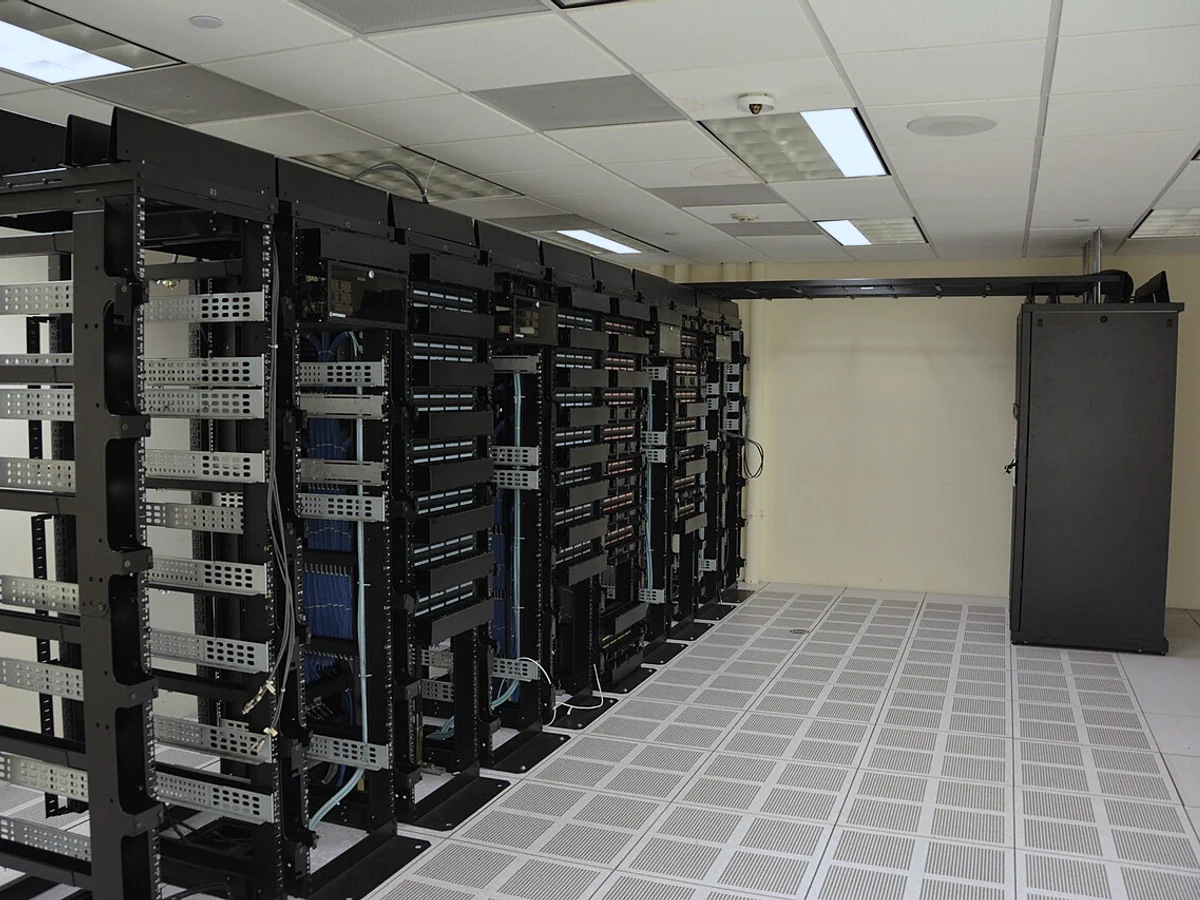 Rows of equipment racks, overhead cable trays and a raised ventilation floor inside a data center
